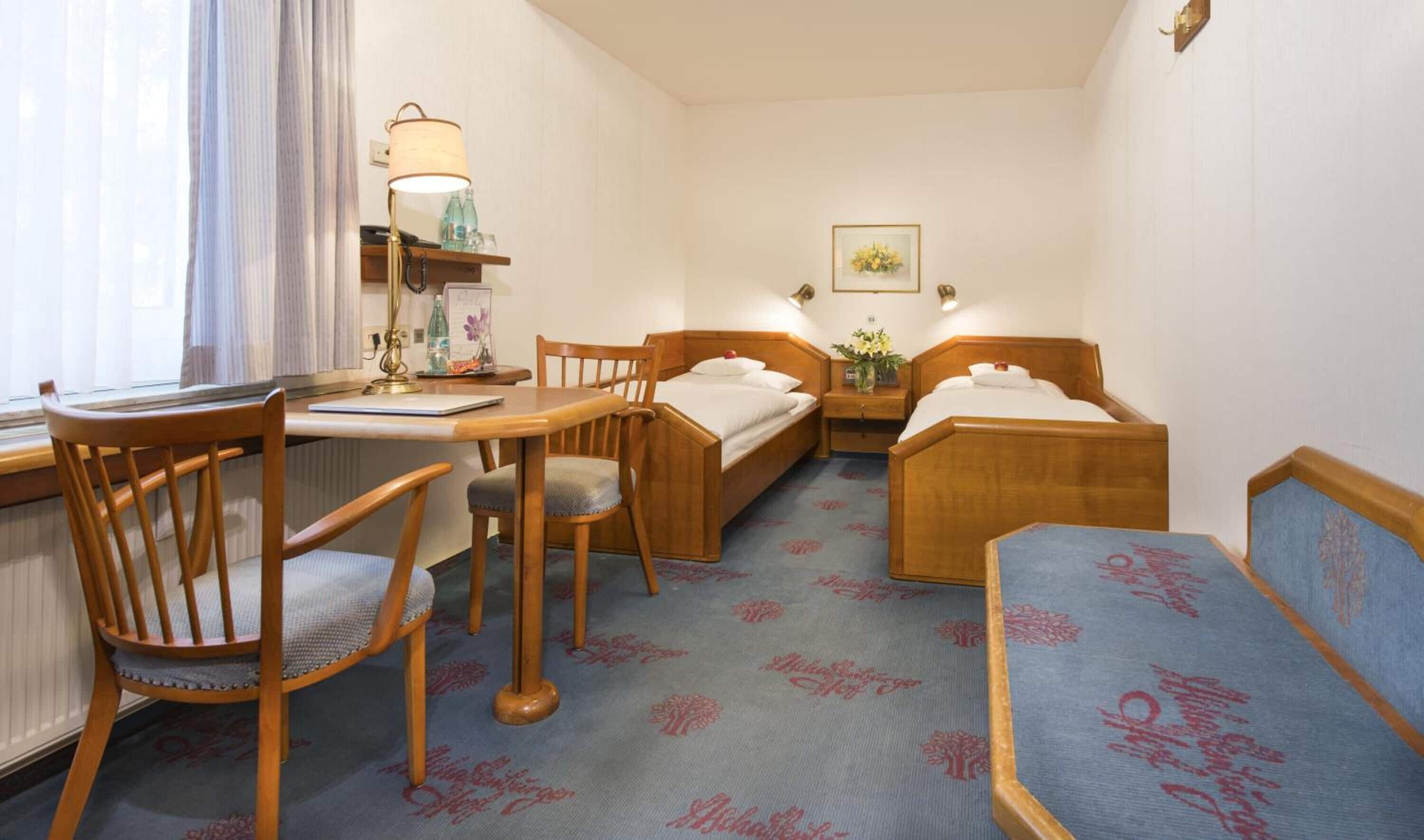 Una habitación de hotel compacta con escritorio, dos camas individuales, una silla y una mesita.