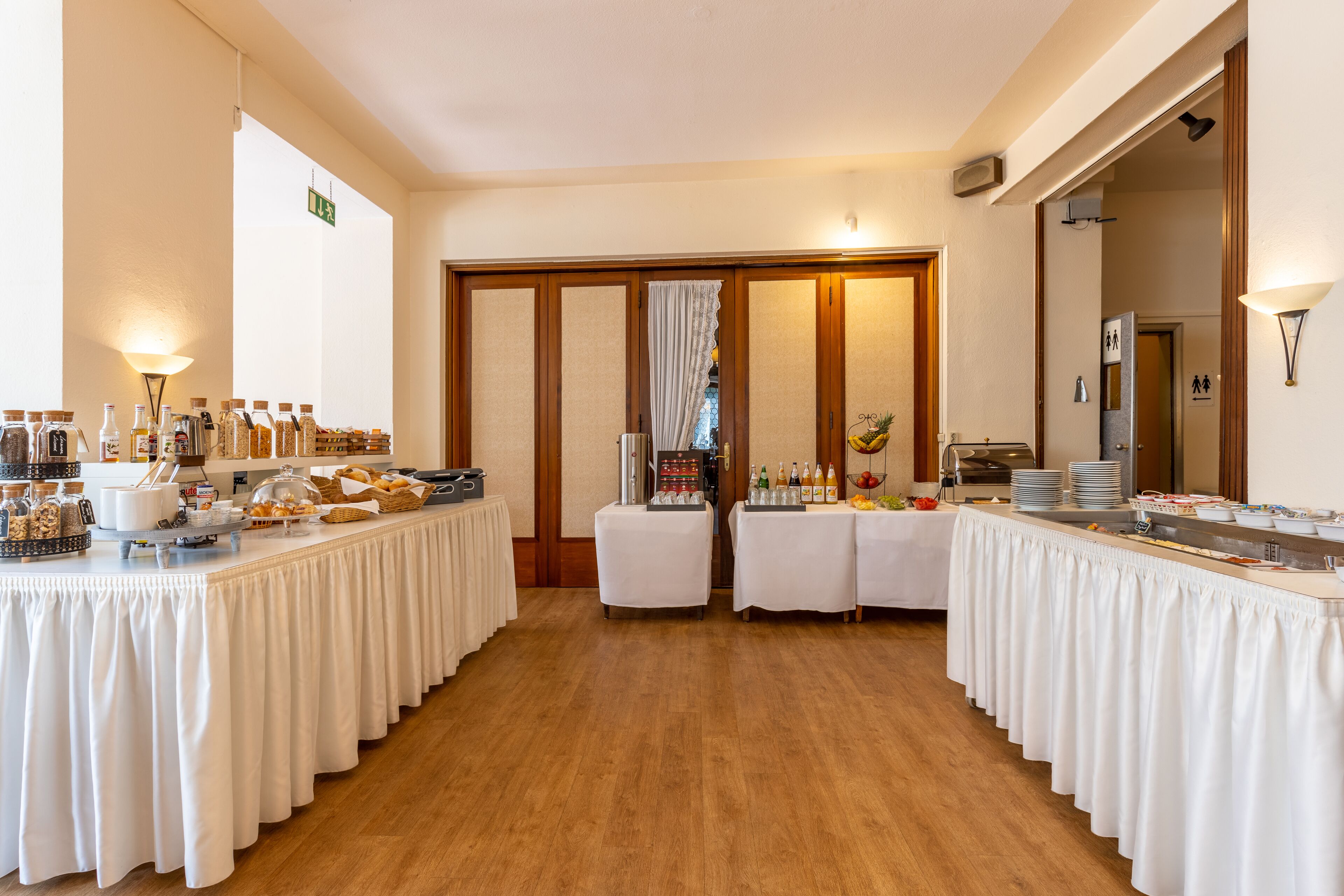 A buffet setup with multiple tables covered in white tablecloths, featuring a variety of food items and beverages.