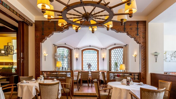 A restaurant with wooden tables and chairs, a large chandelier, and decorative windows. - TRIP INN Hotel Aschaffenburger Hof (Aschaffenburg)