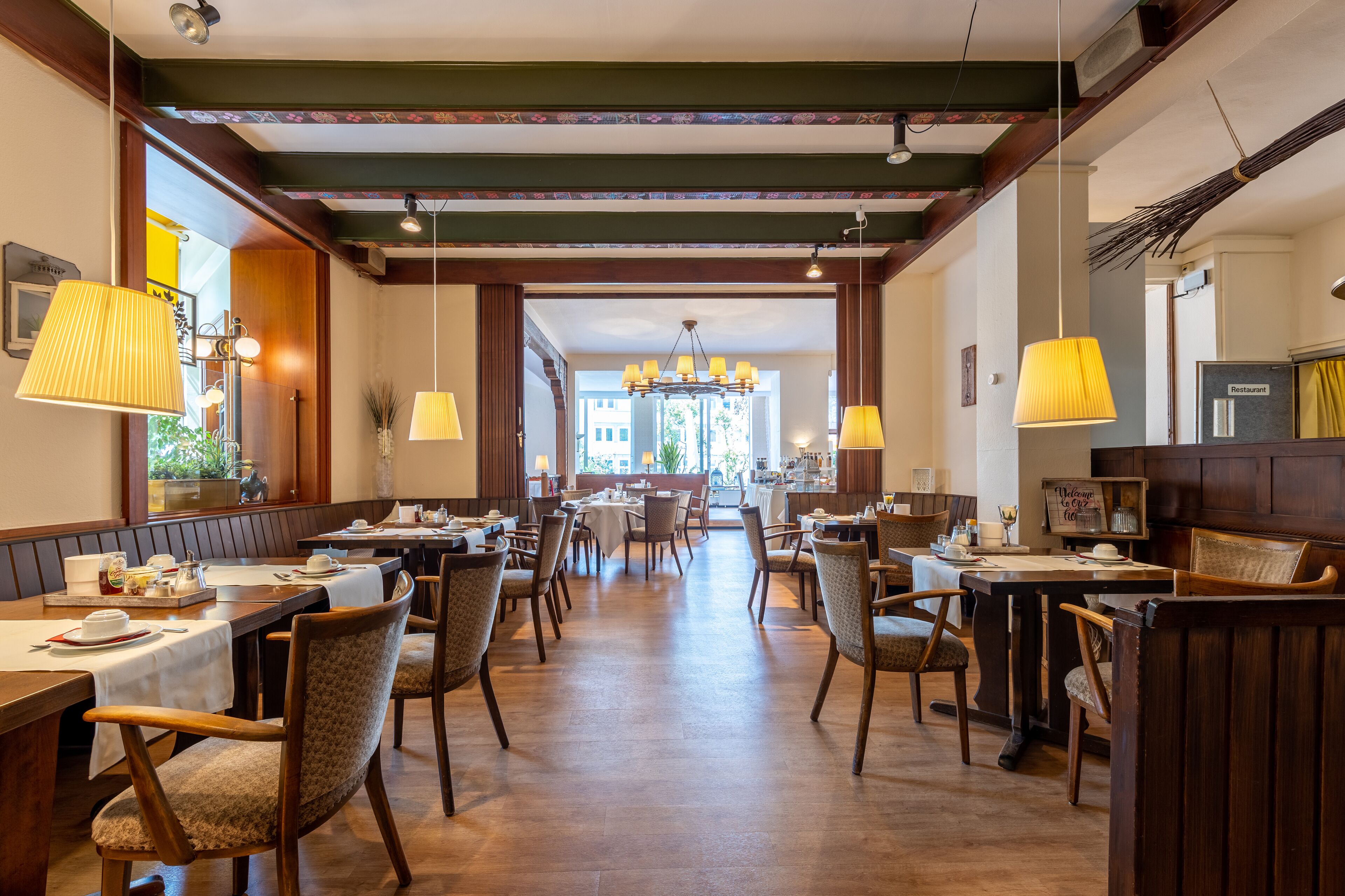 Ein Restaurant mit Holztischen und -stühlen, einer Chandelüster und Blick auf die Straße.