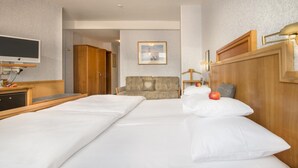 A hotel room with a large bed, a desk with a television, a sofa, and a wall-mounted lamp. - TRIP INN Hotel Aschaffenburger Hof (Aschaffenburg)