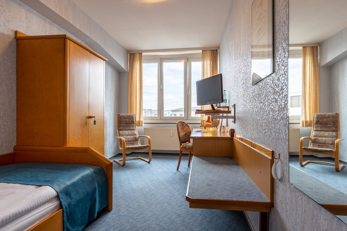 A hotel room with a bed, a desk with a computer, two chairs, and a large mirror.