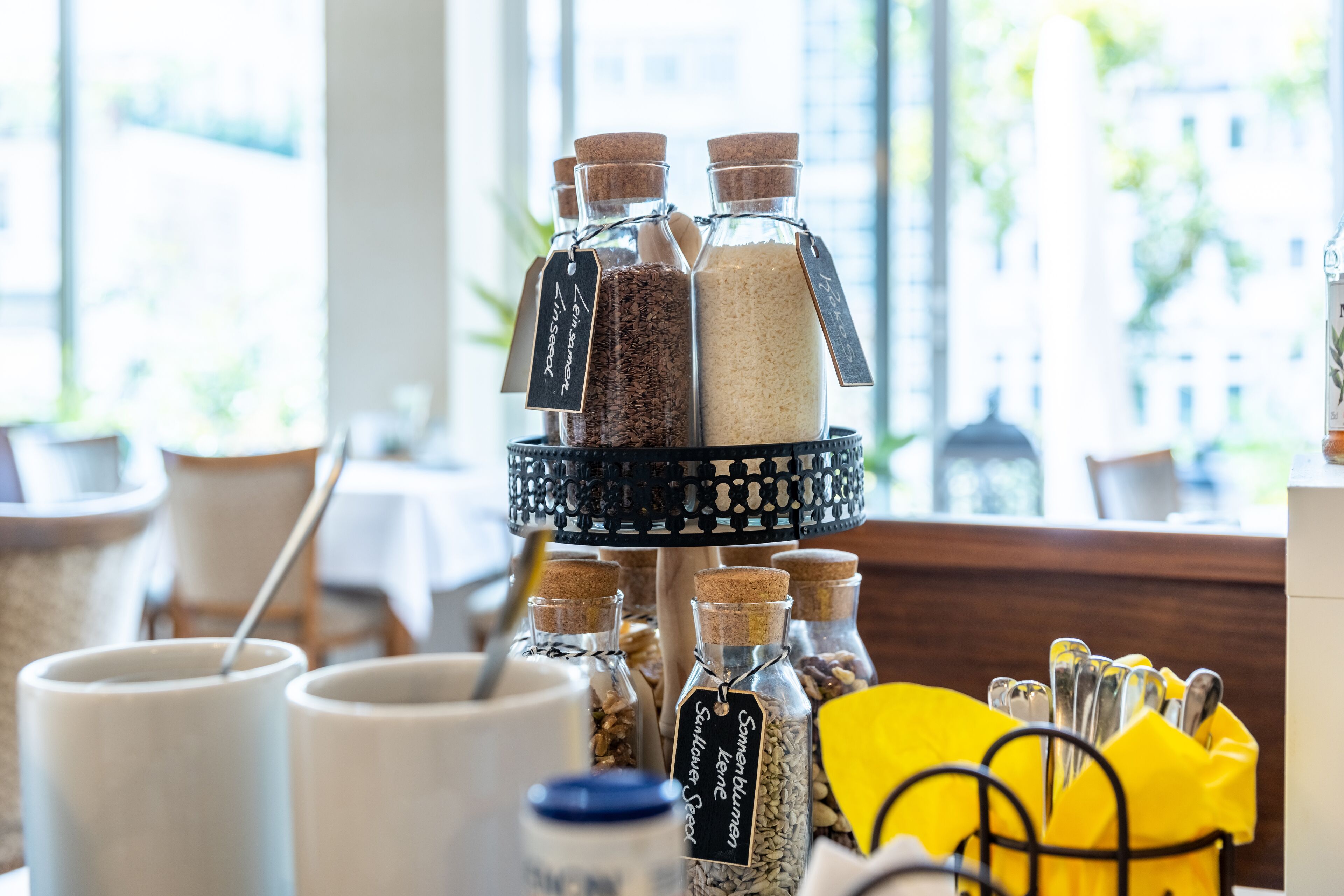 Une étagère à plusieurs niveaux où sont disposés des bocaux en verre avec des étiquettes, un porte-serviettes jaune et une cuillère dans une tasse blanche.