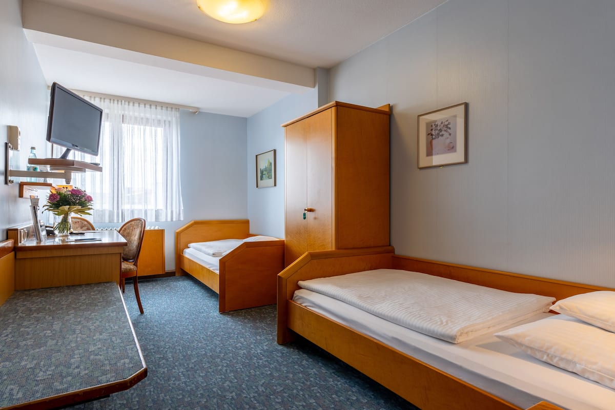 A hotel room with a single bed, a desk with a chair, a television, and a wardrobe.