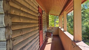 En inglasad veranda med trägolv, ett bord och stolar, en röd dörr och utsikt över träd.