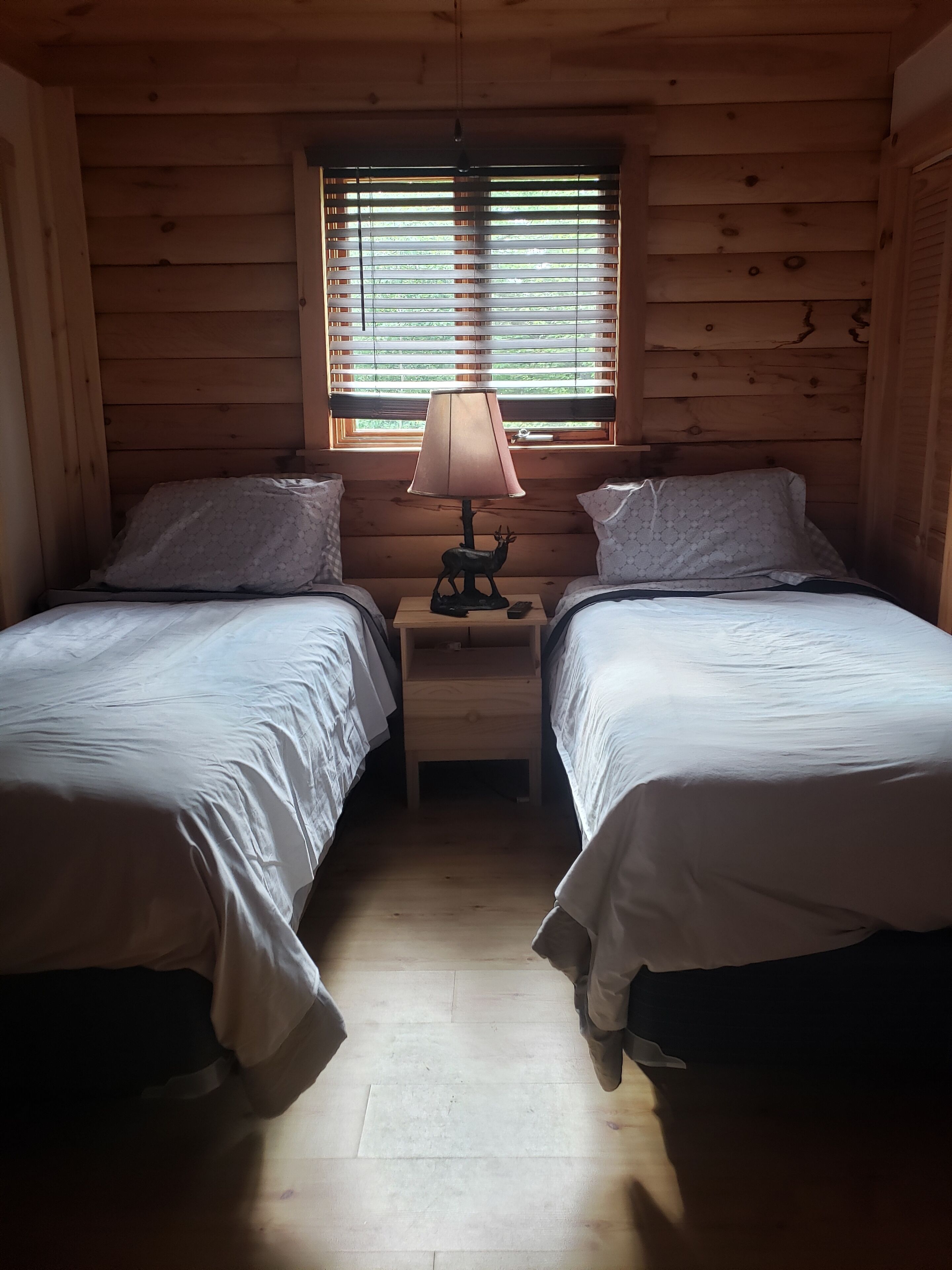A cabin room with two beds, a nightstand with a lamp, and a window with blinds.