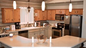 A kitchen with wooden cabinets, stainless steel appliances, a large island with stools, and pendant lighting.