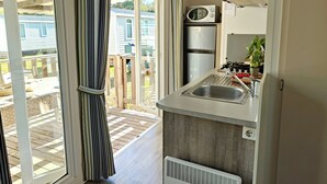A modern kitchen with a built-in microwave, refrigerator, and sink. There is a sliding glass door leading to an outdoor patio area. - Greenchalets Glamping Argeles sur mer (Argelès-sur-Mer)