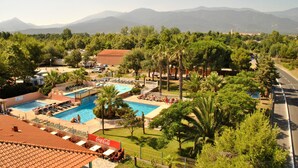 A resort with multiple swimming pools, palm trees, and a mountainous backdrop. - Greenchalets Glamping Argeles sur mer (Argelès-sur-Mer)