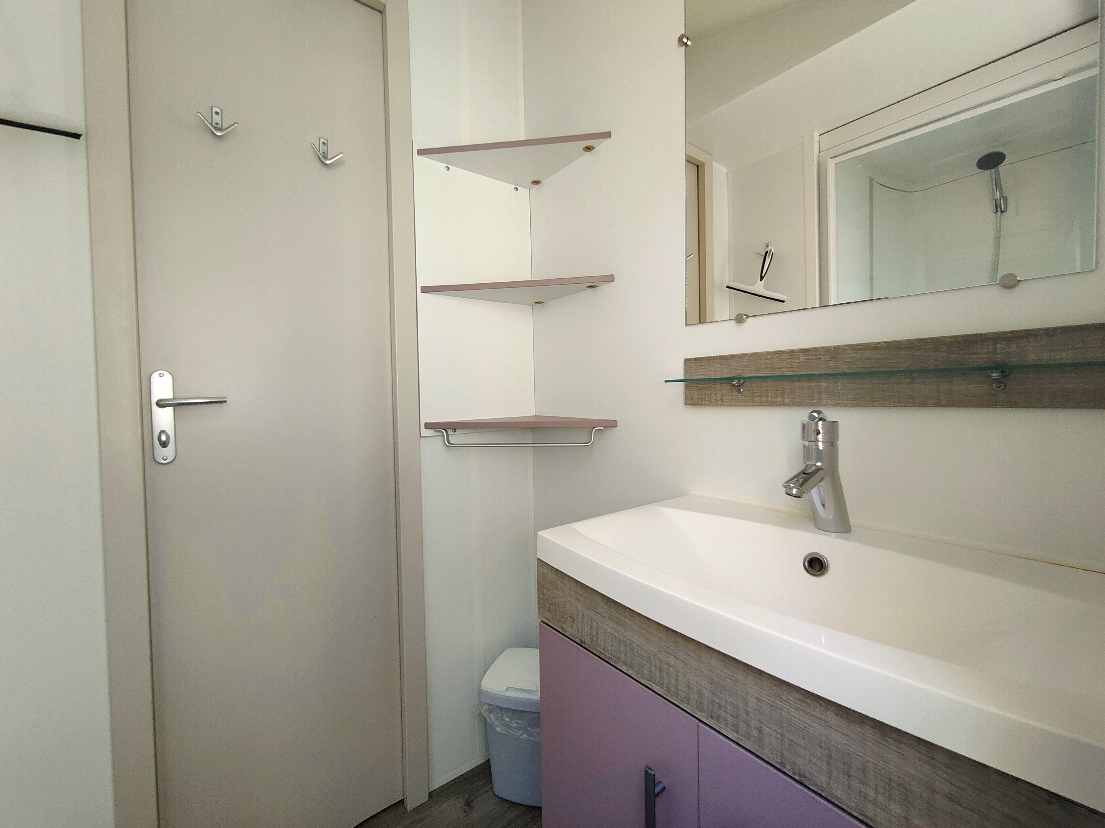 A bathroom with a white sink, a mirror, and three shelves above it.