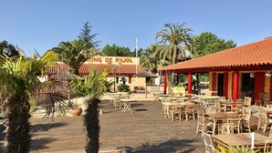 An outdoor dining area with wooden tables and chairs, surrounded by potted plants and a wooden deck. - Greenchalets Glamping Argeles sur mer (Argelès-sur-Mer)