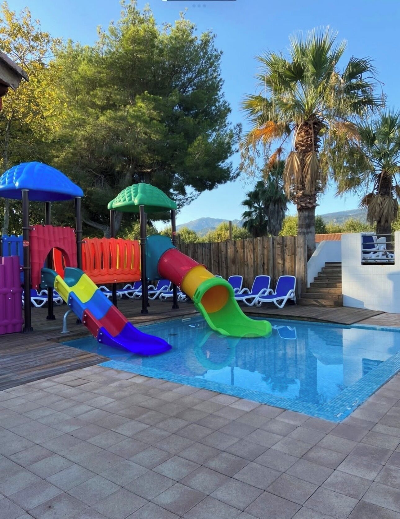 Piscina com escorregador colorido e cadeiras de descanso.