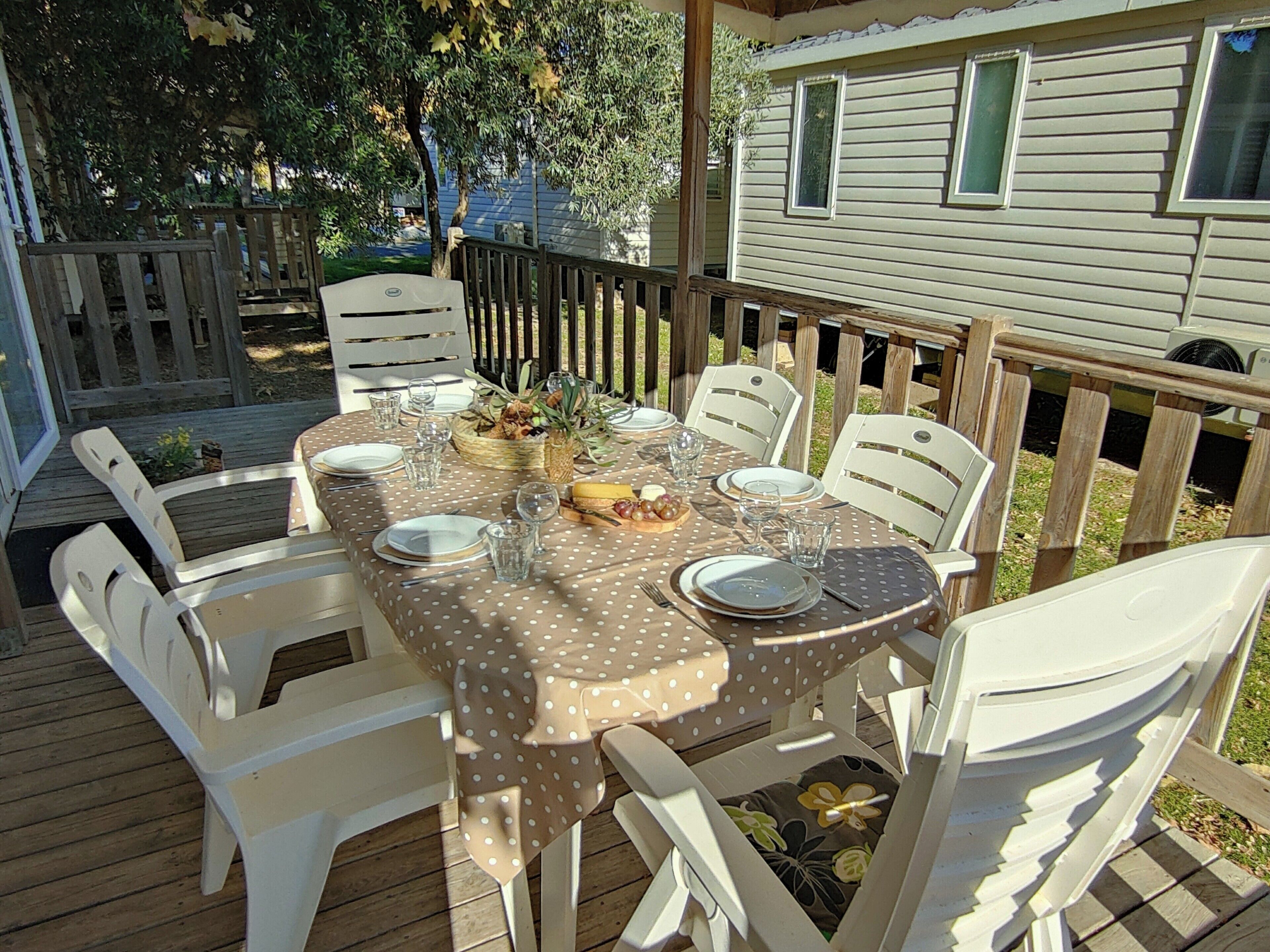 A dining table set outdoors with white chairs, a polka dot tablecloth, and a basket of fruit.
