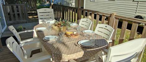 A dining table set outdoors with white chairs, a polka dot tablecloth, and a basket of fruit.