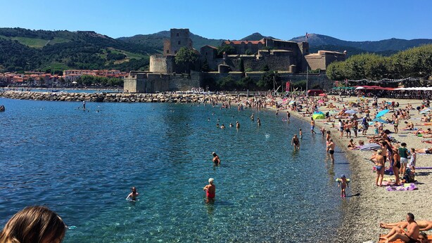A beach with clear water, a castle in the background, and people sunbathing. - Greenchalets Glamping Argeles sur mer (Argelès-sur-Mer)