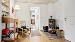 Een gezellige kamer met een houten stoel, een tafel met boeken, een lamp, een open haard en een deur naar een andere kamer.