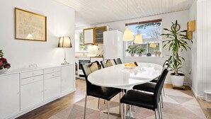 Een moderne keuken met witte kasten, een witte eettafel met zwarte stoelen en hanglampen.