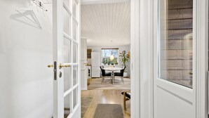 Een gang die uitkomt in een eetgedeelte met een tafel, stoelen, een koelkast en een raam met jaloezieën.