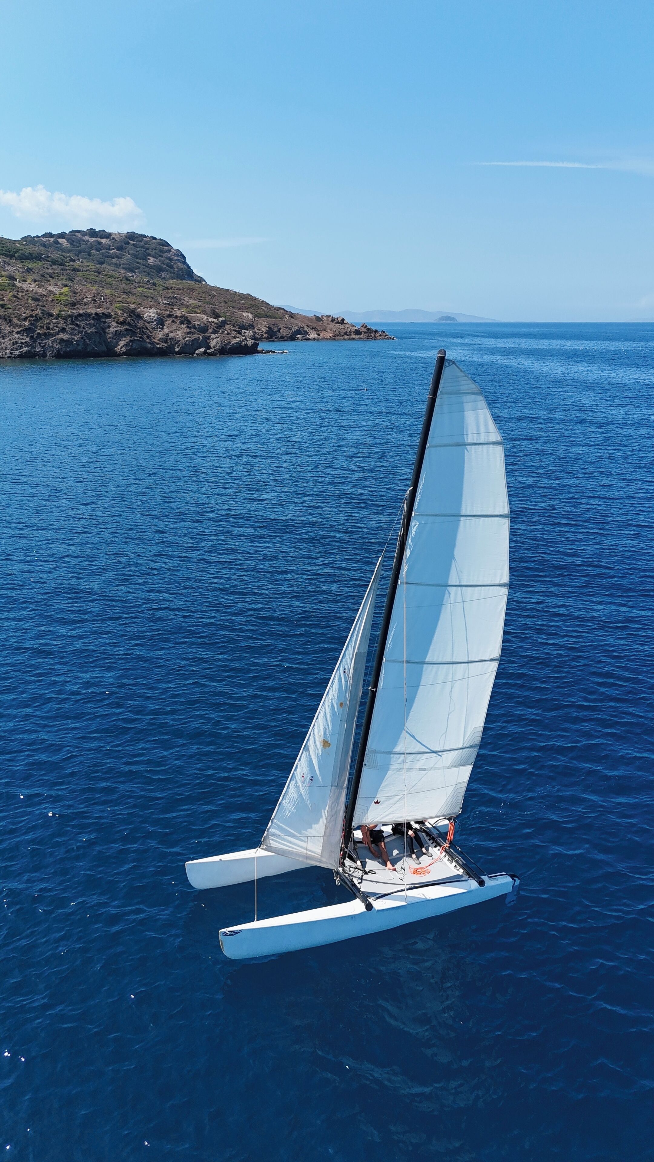 Un velero con una sola vela sobre un mar en calma.