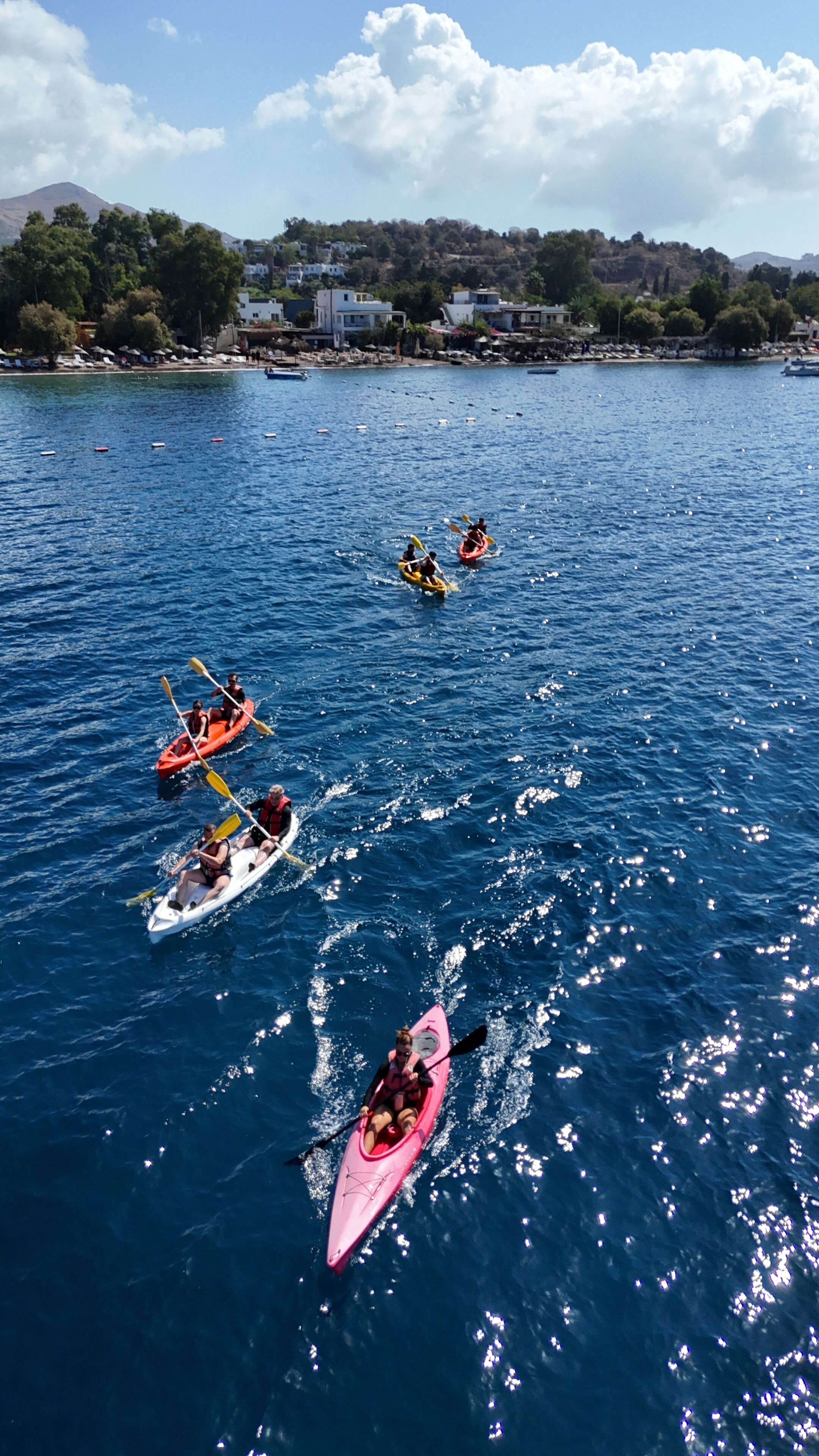 A group of kayaks on a calm body of water with a clear sky and distant buildings.