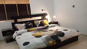 Et moderne soveværelse med en stor seng, et natbord og et vindue med persienner.