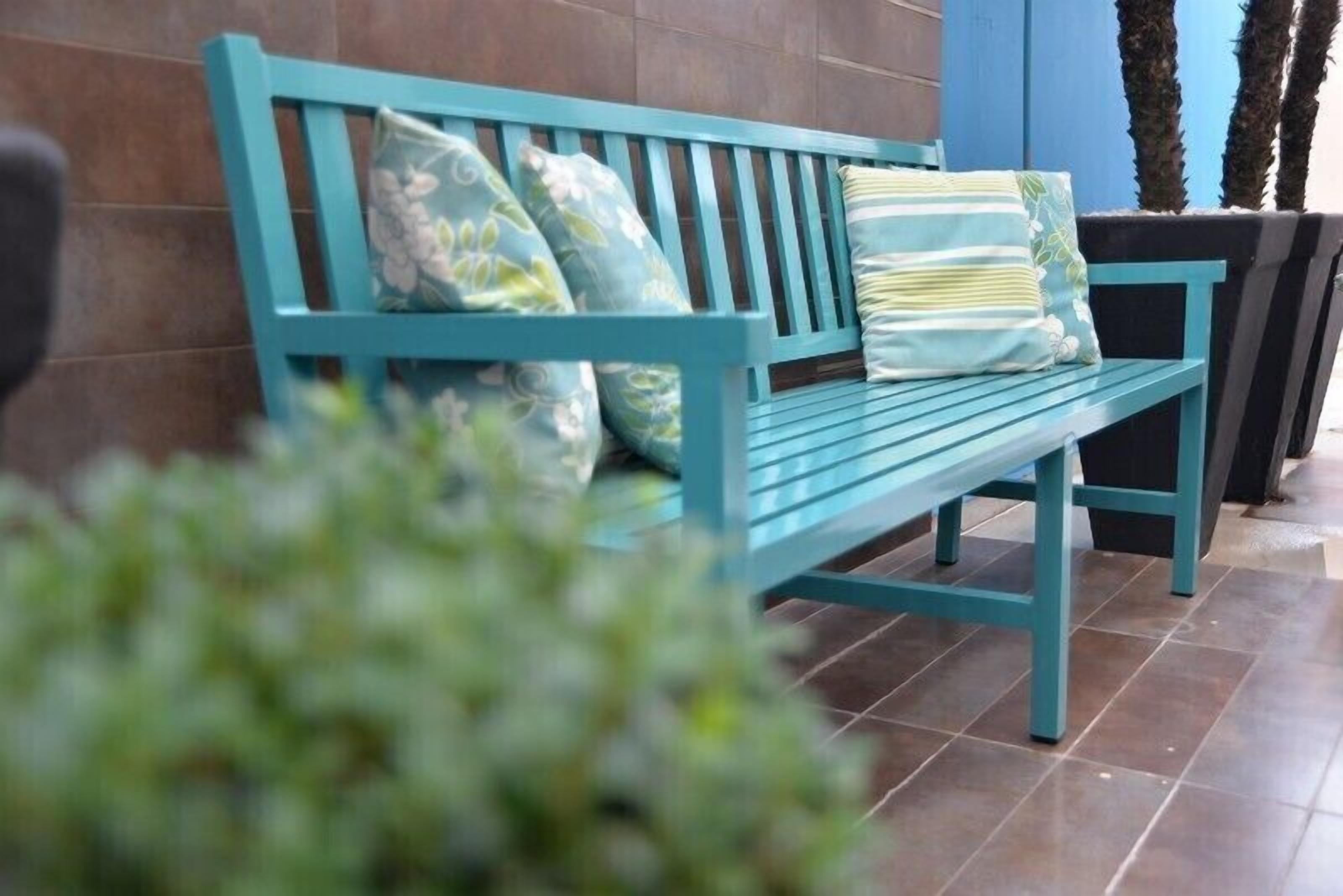 A teal-colored bench with floral-patterned cushions against a tiled wall.