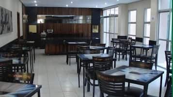A restaurant with multiple tables and chairs, a counter, and a kitchen area.