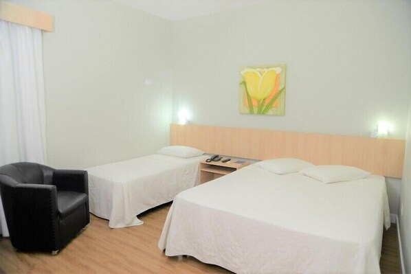 Una habitación de hotel con dos camas individuales, un sillón negro, una mesita de noche con lámpara y un cuadro en la pared.