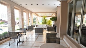 Een overdekt terras met wicker meubels, een centrale bank en een groot raam.