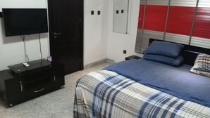 A bedroom with a bed, a TV on a stand, a wardrobe, and a window with blinds. - The Gold (Lekki)