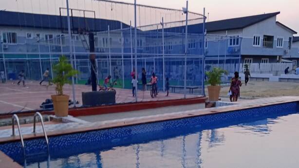 A swimming pool with a tiled edge, a metal ladder, and a few potted plants. - The Gold (Lekki)