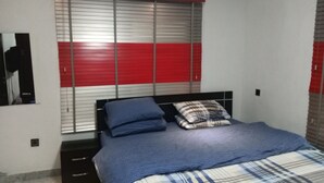 A bedroom with a bed, a nightstand, a dresser, a window with blinds, and an air conditioning unit. - The Gold (Lekki)