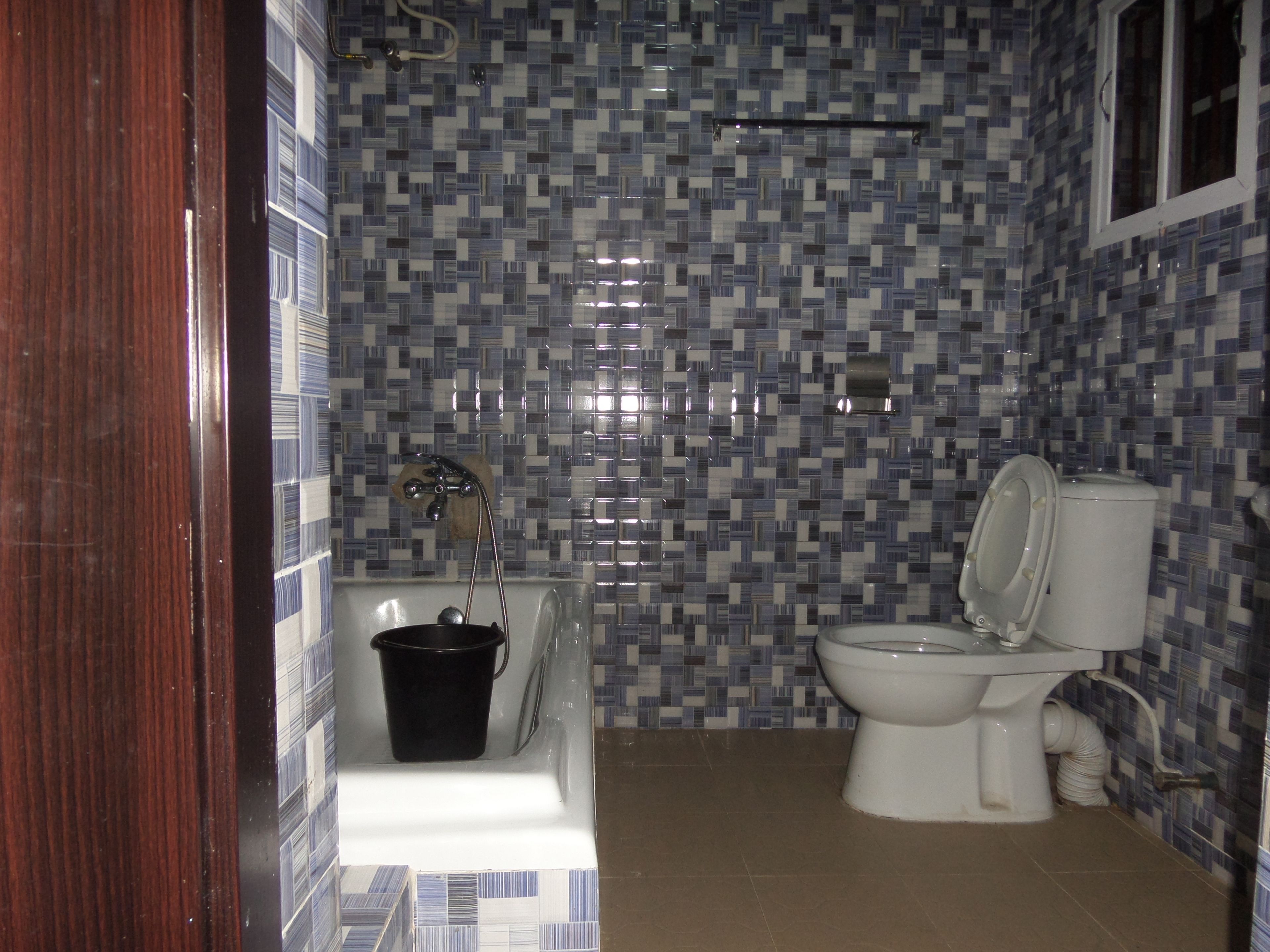 A bathroom with a bathtub, toilet, and a black bucket.
