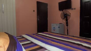 Un dormitorio con cama, ventilador, televisión y refrigerador.