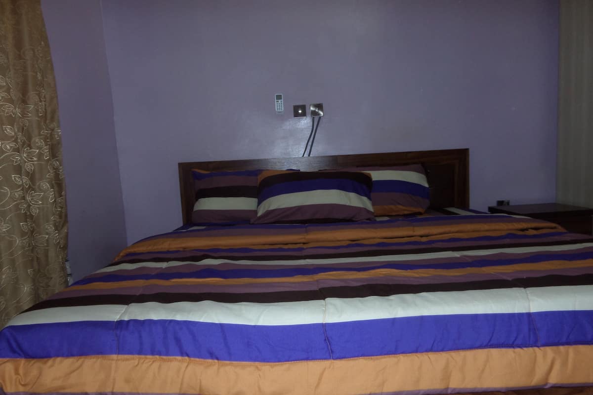 A bed with a striped bedspread, a wooden headboard, and a wall-mounted power outlet.