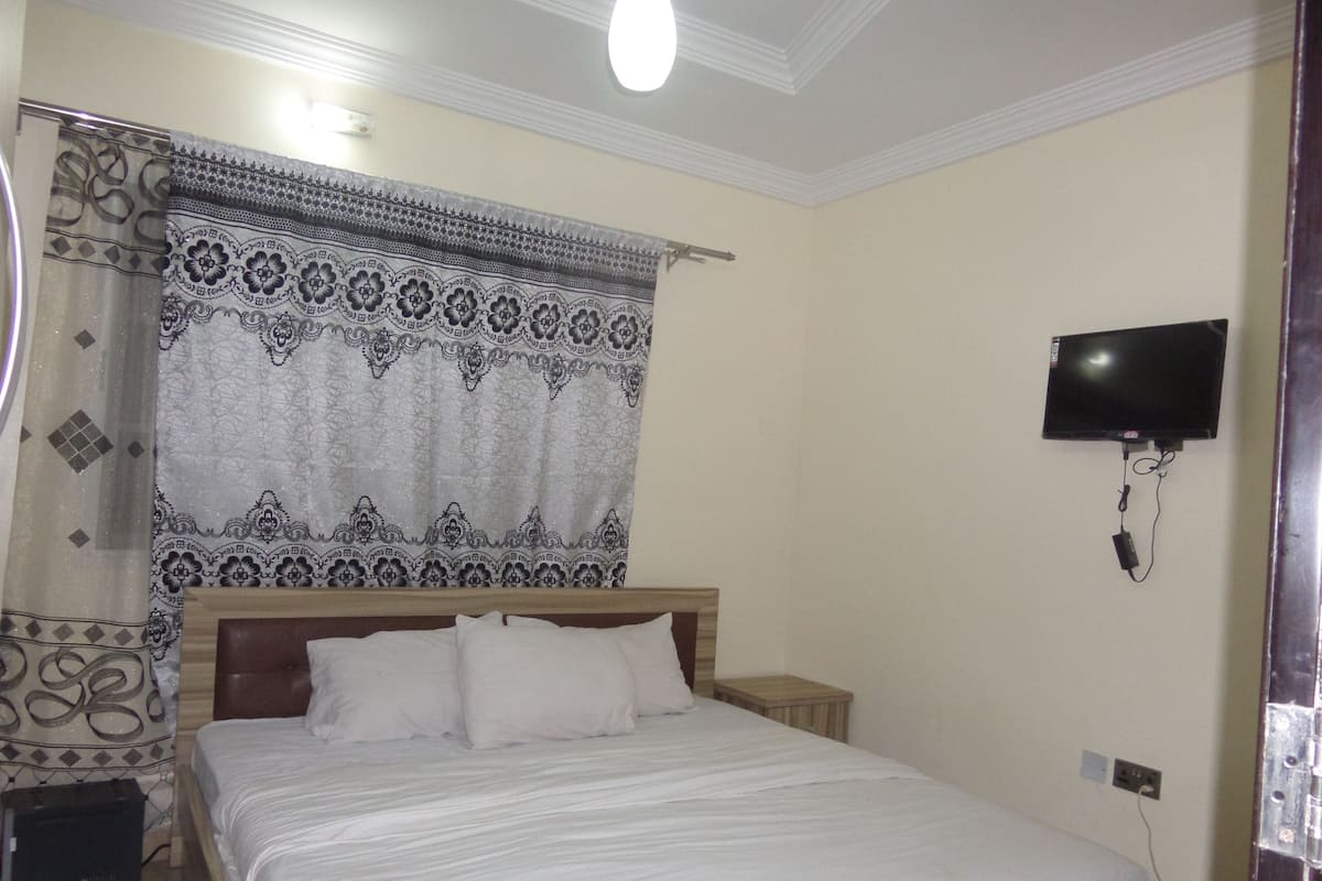A bedroom with a bed, a television mounted on the wall, and a patterned curtain.