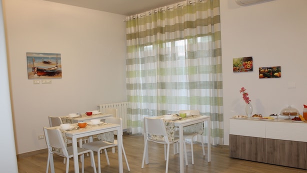 A dining area with two white tables and chairs, a buffet counter with food, and a window with striped curtains.