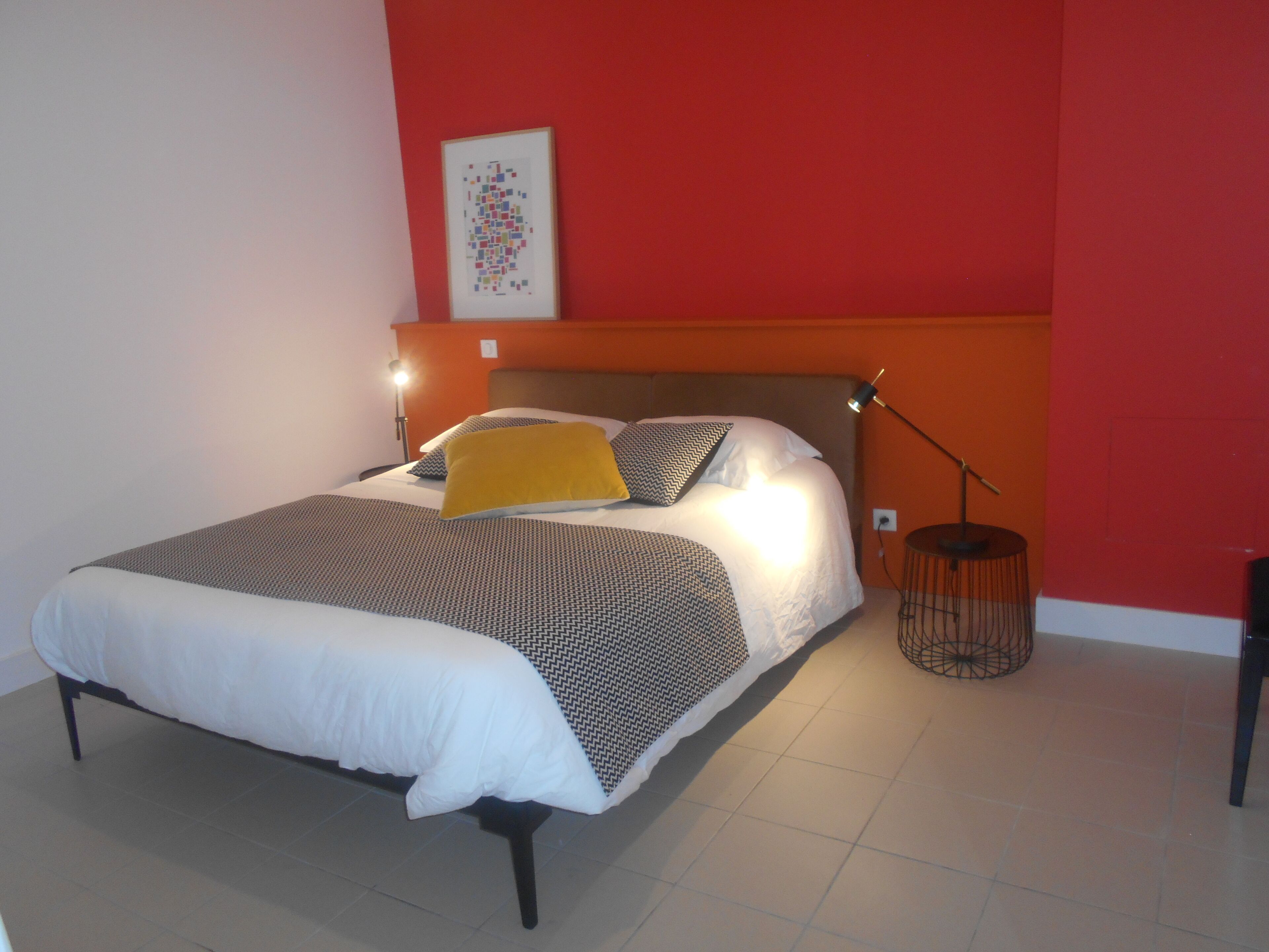 A neatly made bed with a patterned bedspread and pillows, a bedside lamp, and a framed picture on the wall.