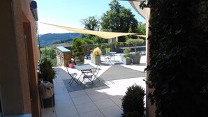 An outdoor patio with a table and chairs, surrounded by potted plants and a view of the landscape.