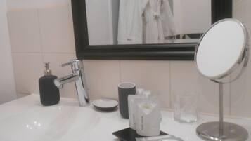 Un baño con lavamanos blanco, espejo, dispensador de jabón, taza y una pequeña bandeja con un paquete.