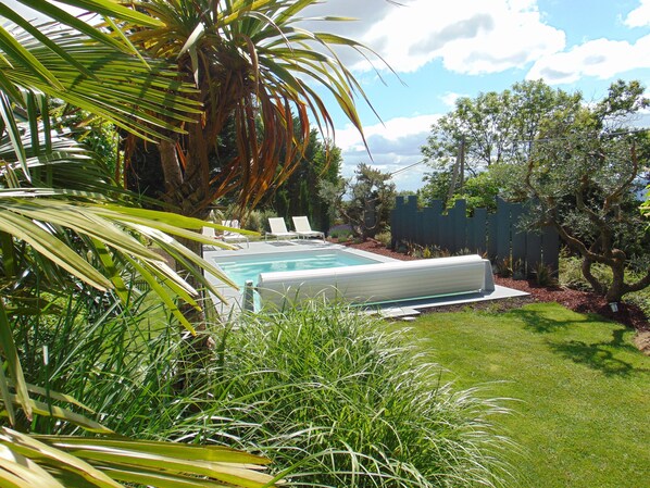 Un giardino sul retro con piscina, sedie a sdraio e diverse piante.