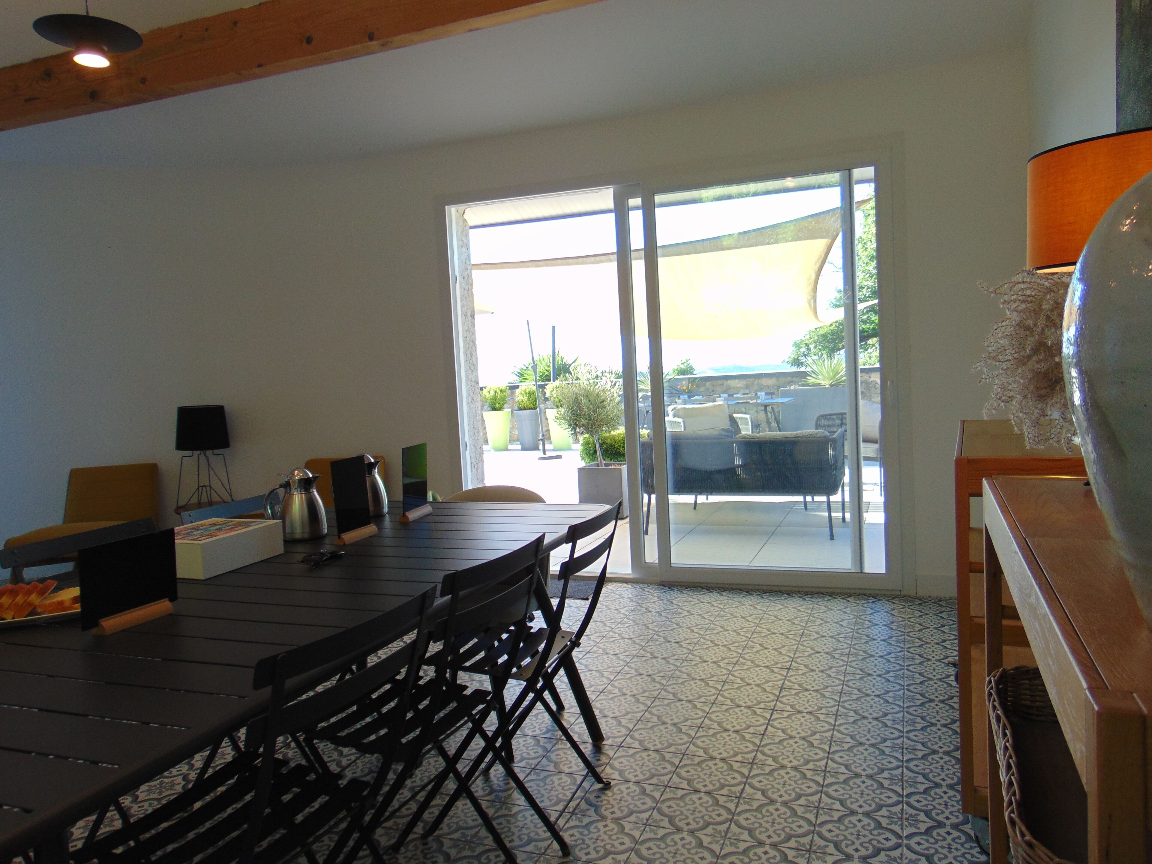 Un comedor con mesa y sillas, una cafetera, una lámpara y vistas a un patio exterior por una puerta de cristal.