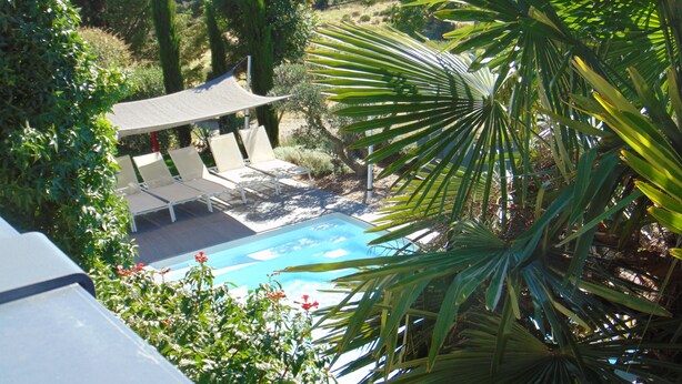 A pool with lounge chairs and a shaded area, surrounded by greenery.