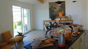 A breakfast area with a table, chairs, a coffee machine, a fruit bowl, and a fruit juice dispenser.