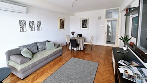 A living room with a sofa, a dining table with chairs, and a TV. - Apartment Fran Green & Blue (Rijeka)