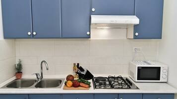 A kitchen with blue cabinets, a white countertop, a sink, a stove, a microwave, and a potted plant.
