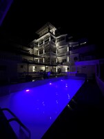 Um edifício com várias andares, varandas e uma piscina iluminada em azul.