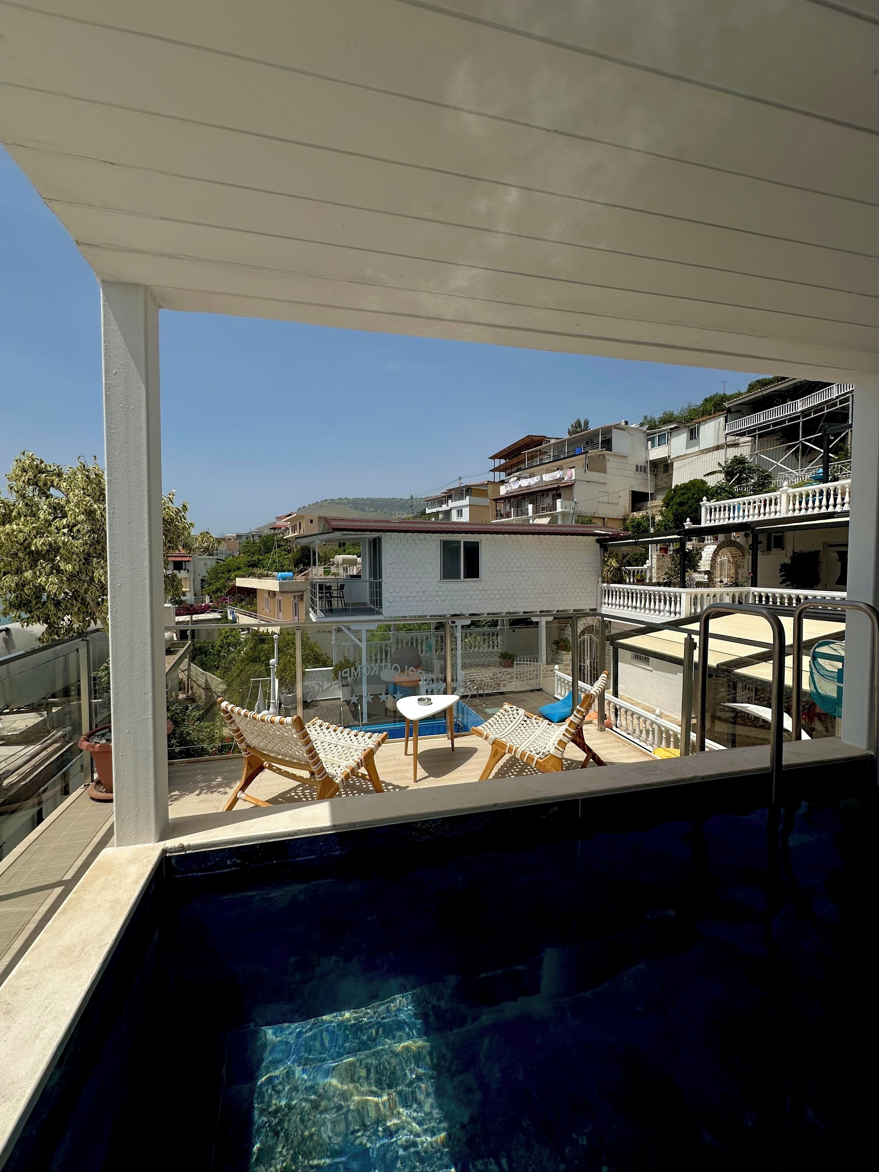 A balcony with a pool, wicker chairs, and a view of a residential area.