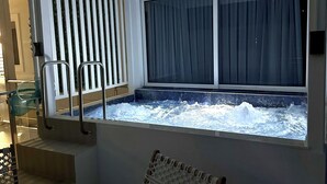 A modern room with a large window, a built-in hot tub, and a macramé chair.