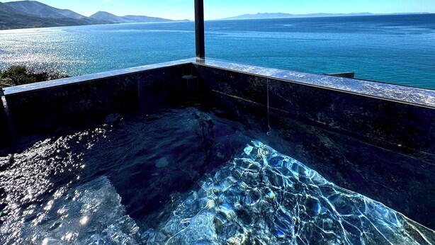 A clear view of a swimming pool with a view of the ocean and mountains in the background.